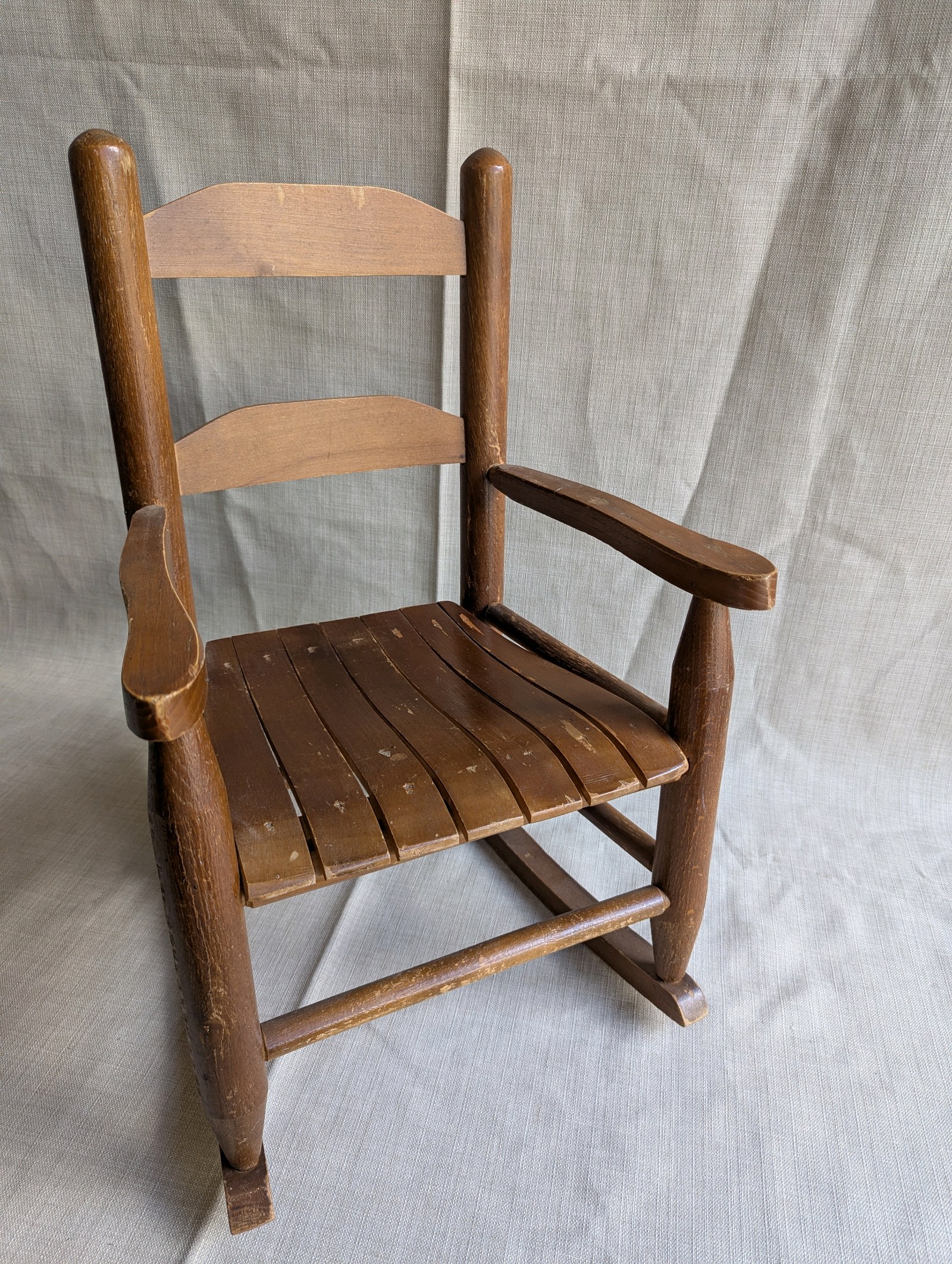 Vintage wooden childs rocking chair, slat seat, ladder-back design, and a rustic brown finish